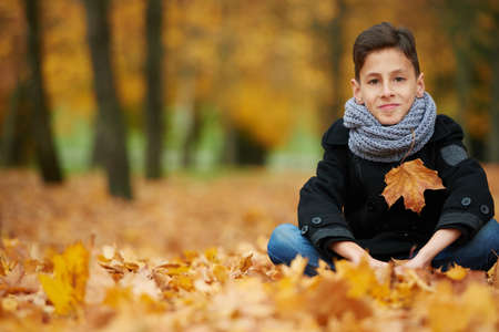 young boy sitting on yellow leaves in the park