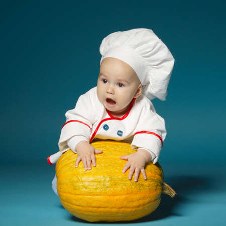 little funny baby with cook costume holds pumpkinの写真素材