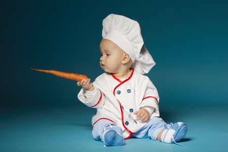 little funny baby with cook costume holds carrotの写真素材