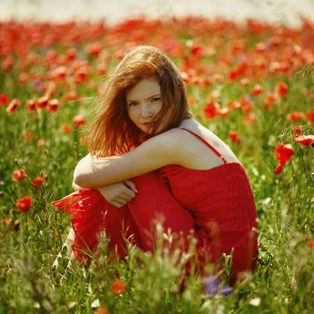 young red haired beautiful girl in poppy fieldの写真素材