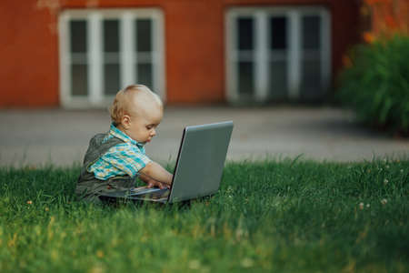 photo of cute little boy with laptop on grassの写真素材