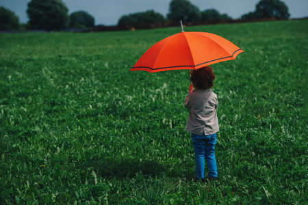 little stylish boy with red umbrella in summer fieldの写真素材