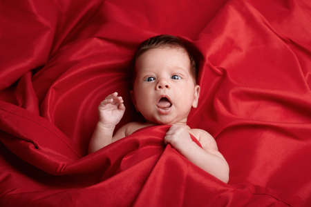 photo of beautiful baby lying on red silk backgroundの写真素材