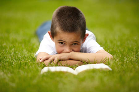 little happy boy reading book on the grassの写真素材