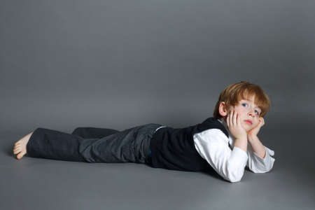 photo of little funny boy lying on dark backgroundの写真素材