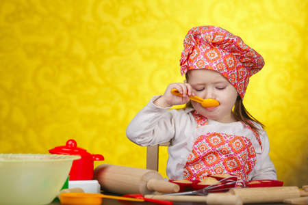 Little baker or cook girl cuts dough for cookies on kitchen with formの写真素材