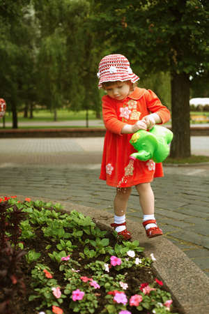 Cute curly girl watering flowers in the gardenの写真素材