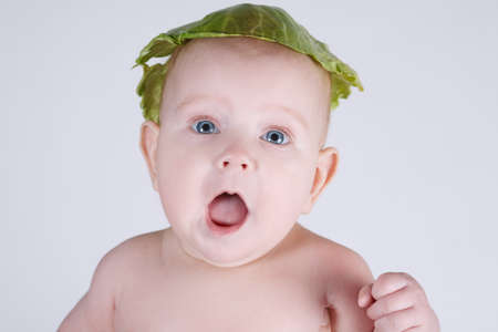 baby with cabbage leaf on his headの写真素材