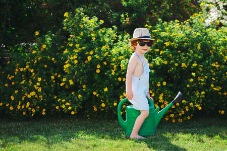 photo of cute little boy with water can in gardenの写真素材
