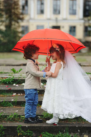 Two funny little bride and groom under the red umbrellaの写真素材