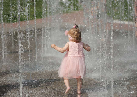 little girl plays with water in summer fountainの写真素材