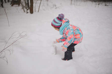girl makes snowman in winter parkの写真素材