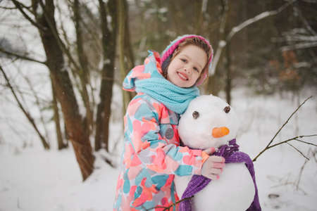 girl makes snowman in winter parkの写真素材