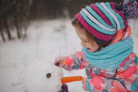 girl makes snowman in winter parkの写真素材