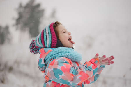 little girl catching snowflakes in winter parkの写真素材