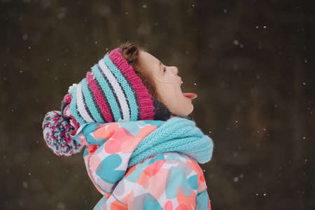 little girl catching snowflakes in winter parkの写真素材
