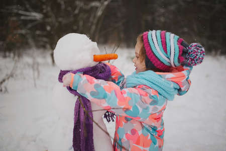 girl makes snowman in winter parkの写真素材
