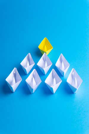 White and yellow paper boat or ship in one direction on blue background. Business for innovative solution concept with selective focusの写真素材