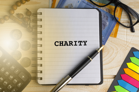 CHARITY inscription written on book with calculator, rosary, coins, banknotes, book, eyeglasses and...