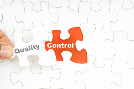 Hand holding piece of jigsaw puzzle with word QUALITY CONTROL. Selective focusの写真素材
