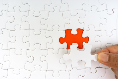 Hand put the last piece of jigsaw puzzle closeup to complete the mission. Selective focus and crop fragmentの写真素材