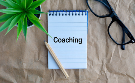 Notepad, flower vase, spectacle, pencil and words COACHING on wooden paper background. Business, education concept and copy space conceptの写真素材