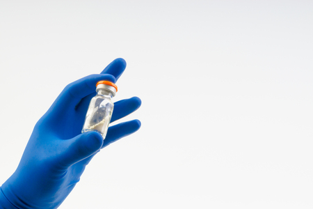 Hand in a blue glove holding medical vial isolated on whiteの写真素材