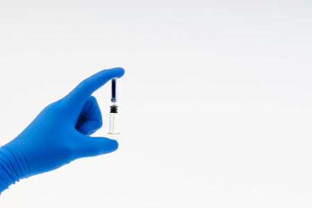 Hand in a blue glove holding syringe isolated on whiteの写真素材
