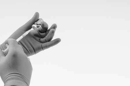 Hand in a blue glove holding syringe and vial on black and whiteの写真素材
