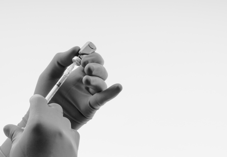Hand in a blue glove holding syringe and vial on black and whiteの写真素材