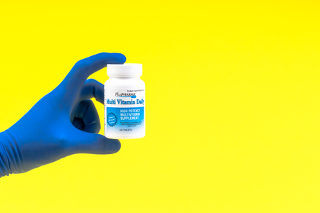 Kuala Lumpur, Malaysia - 21 May, 2109 : Hand in a blue glove holding multivitamin bottle on yellow backgroundのeditorial素材
