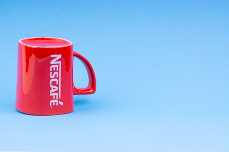 Kuala Lumpur, Malaysia - July 03, 2019:  Promotional red Nescafe mug on blue background. Selective focusのeditorial素材