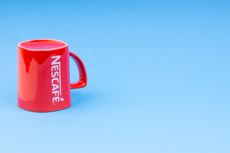 Kuala Lumpur, Malaysia - July 03, 2019:  Promotional red Nescafe mug on blue background. Selective focusのeditorial素材