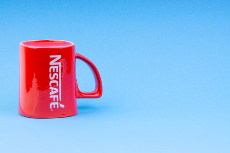 Kuala Lumpur, Malaysia - July 03, 2019:  Promotional red Nescafe mug on blue background. Selective focusのeditorial素材