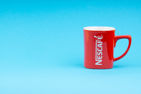 Kuala Lumpur, Malaysia - July 03, 2019:  Promotional red Nescafe mug on blue background. Selective focusのeditorial素材