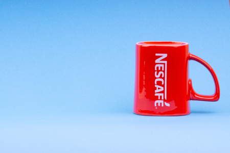 Kuala Lumpur, Malaysia - July 03, 2019:  Promotional red Nescafe mug on blue background. Selective focusのeditorial素材