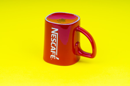Kuala Lumpur, Malaysia - June 24, 2019: Red Nescafe mug isolate on yellow background. Selective focusのeditorial素材