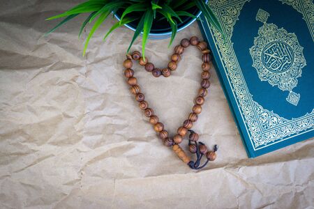Flat lay Holy Quran with arabic calligraphy meaning of Al Quran and tasbih or rosary beads over...