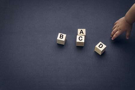 Wooden alphabet cube with words ABCD closeup and children hands on black background. Selective focus...