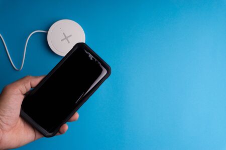 Smartphone charging on a charging pad or dock on blue background.Wireless charging and copy space の写真素材