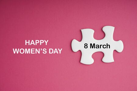 HAPPY WOMEN DAY text with white jigsaw puzzle on pink background.