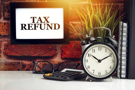 TAX REFUND text with alarm clock, books and vase on brick background. Business, Quotes and Copy Space conceptの写真素材