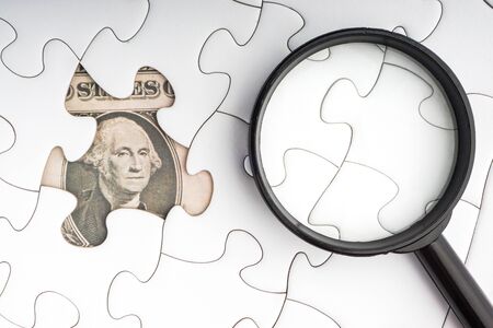 US Dollar banknotes and magnifying glass on white jigsaw puzzle. Business and copy space conceptの写真素材