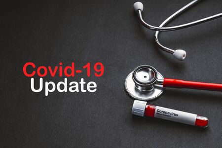 COVID 19 UPDATE text with stethoscope and blood sample vacuum tube on black background. Covid or Coronavirus Conceptの写真素材