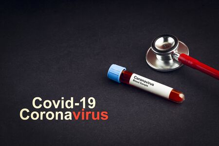 COVID-19 CORONAVIRUS text with stethoscope and blood sample vacuum tube on black background. Covid or Coronavirus Conceptの写真素材