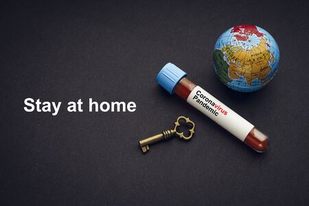 STAY AT HOME text with world globe, key and Blood test vacuum tube on black background. Covid-19 or Coronavirus Conceptの写真素材