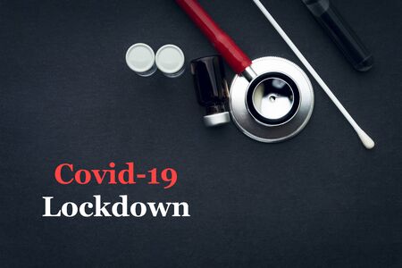 COVID-19 or CORONAVIRUS LOCKDOWN text with stethoscope, medical swab and vial on black background....
