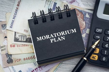 MORATORIUM PLAN text with fountain pen, calculator, currency banknotes and notepad on wooden background. Business and economic conceptの写真素材