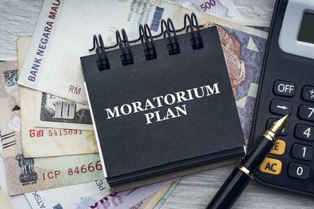 MORATORIUM PLAN text with fountain pen, calculator, currency banknotes and notepad on wooden background. Business and economic conceptの素材 [FY310144371755]