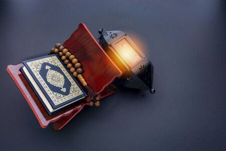 Holy Al Quran with written arabic calligraphy meaning of Al Quran, lantern lamp and rosary beads or tasbih on black background.の写真素材